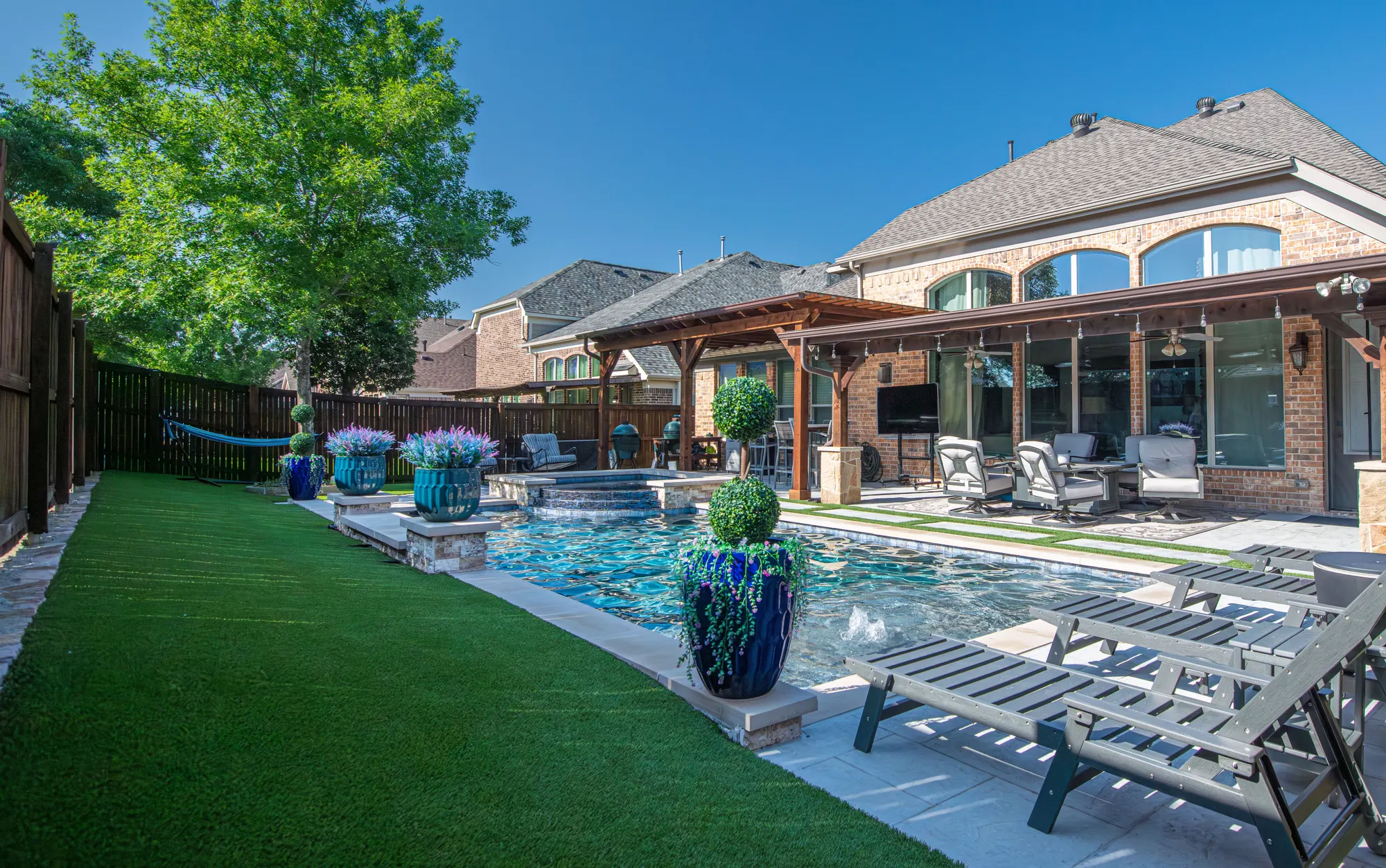 Kyle-area backyard with an artificial turf lawn next to a pool and a covered patio
