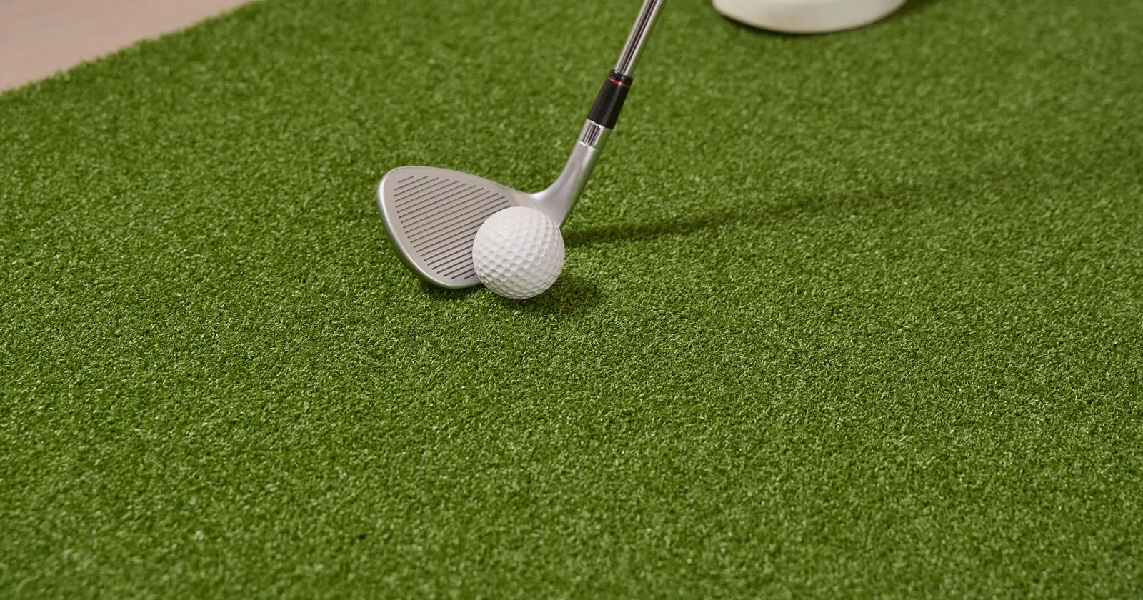 Wedge set behind a golf ball on artificial turf fringe